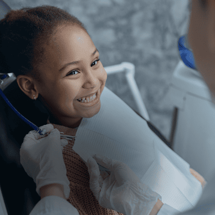 Uma menina sorridente recebendo tratamento odontológico com uma dentista ao fundo