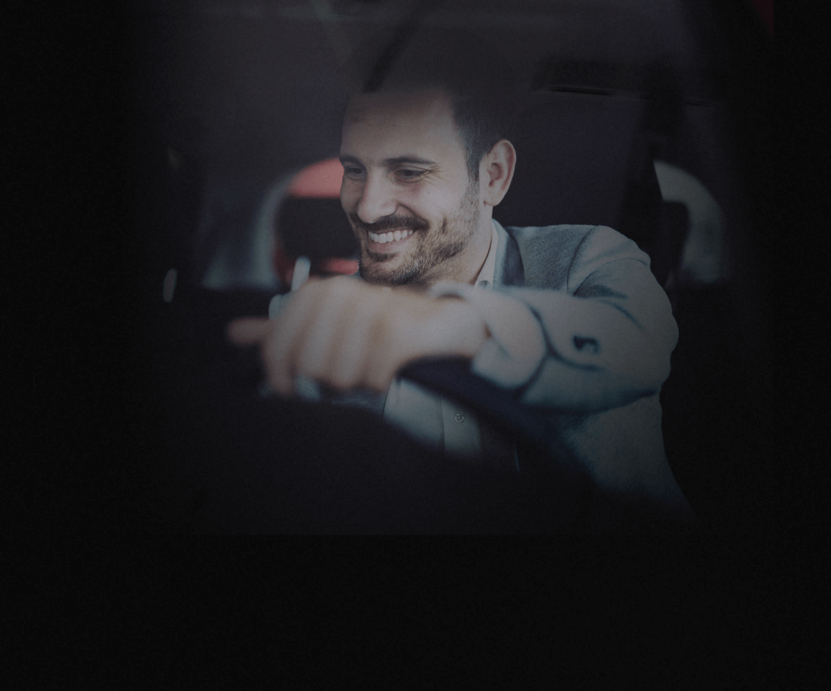 Motorista Uber pro sorridente dirigindo um carro, visto de fora do carro.